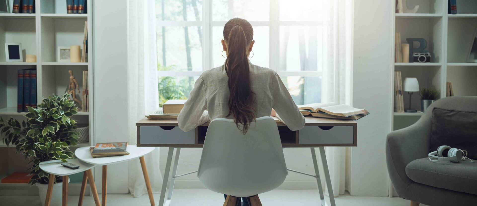 A woman is sitting at a desk in front of a window.