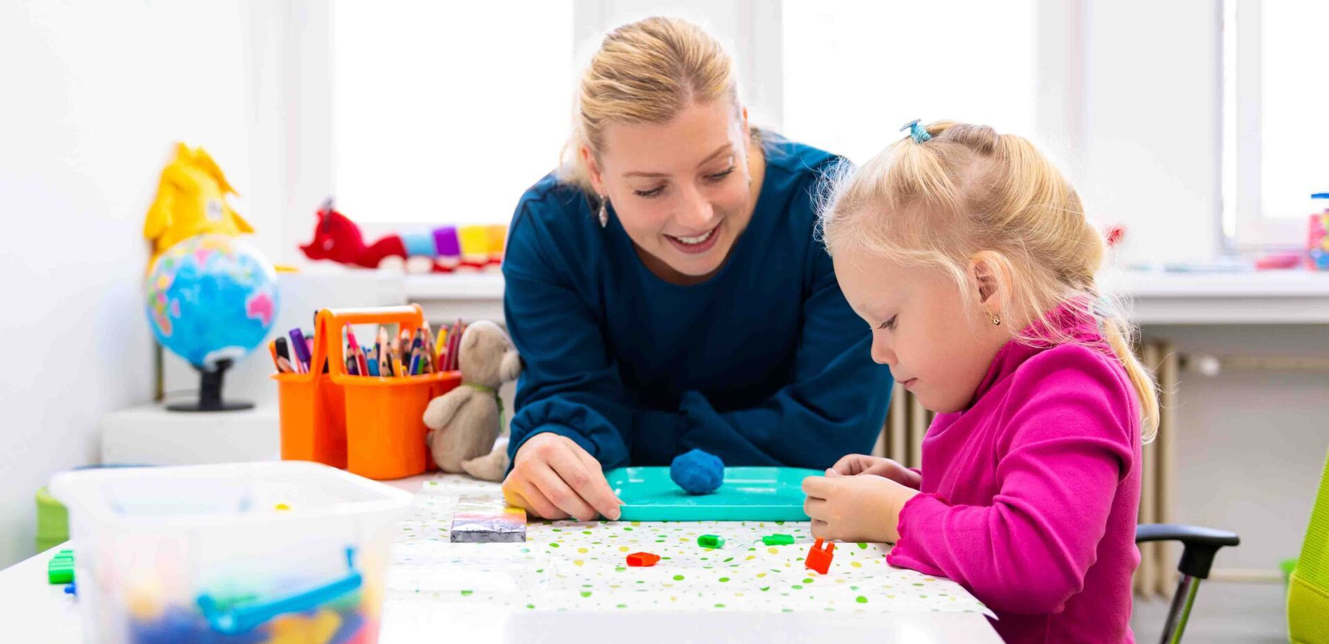 A woman and a little girl are playing with clay at a table.