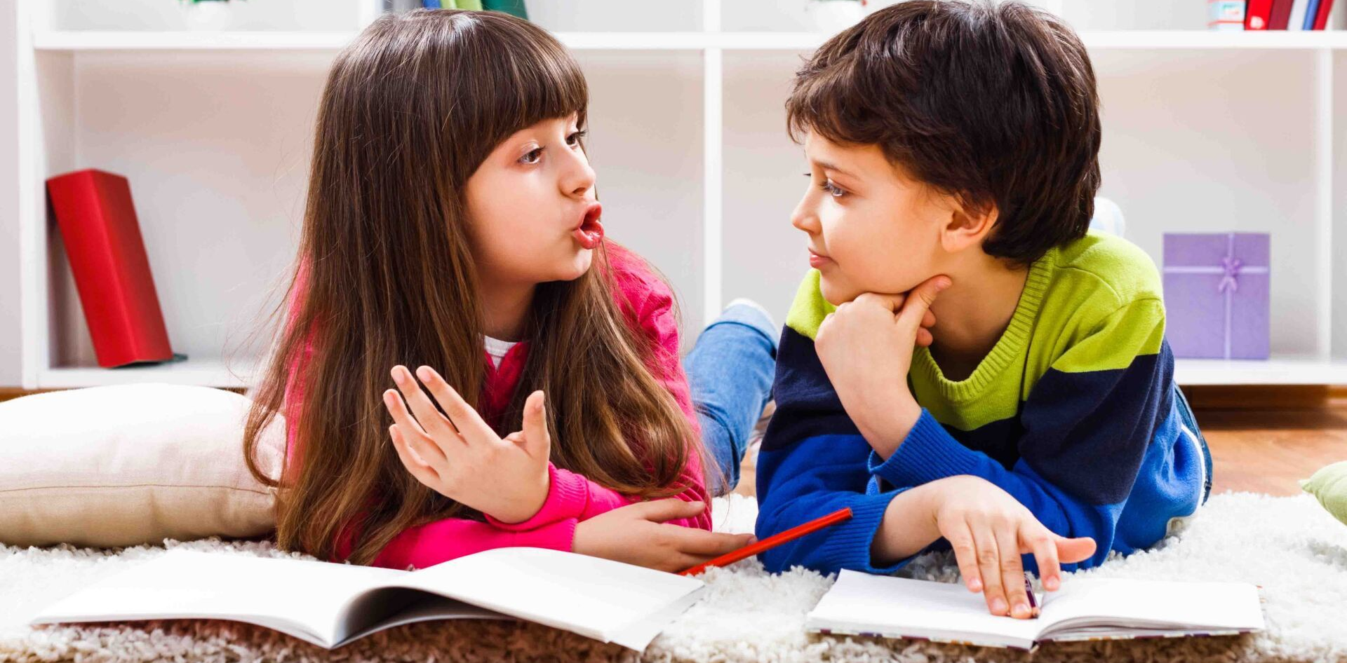 A boy and a girl are laying on the floor talking to each other.