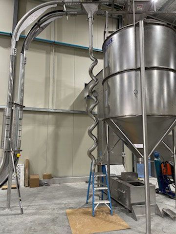 A large stainless steel silo with a spiral conveyor belt attached to it in a factory.