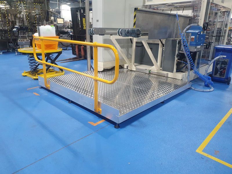 A machine is sitting on a platform in a factory with a yellow railing.