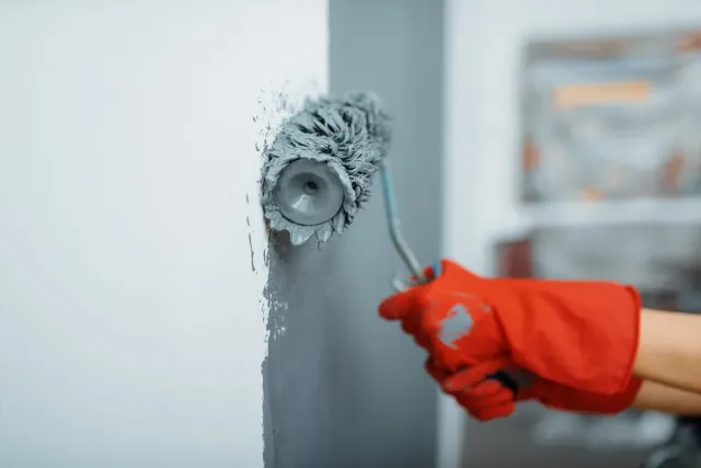 A person is painting a wall with a paint roller.