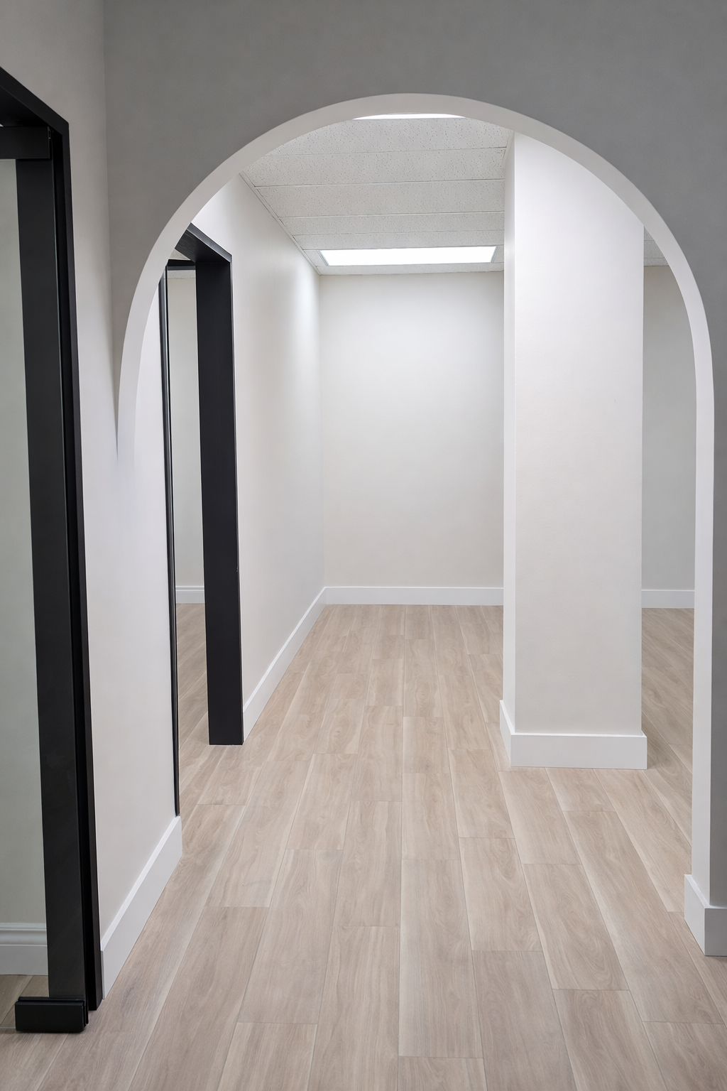Couloir vide avec parquet clair, murs blancs et une arche arrondie ouvrant sur une petite pièce