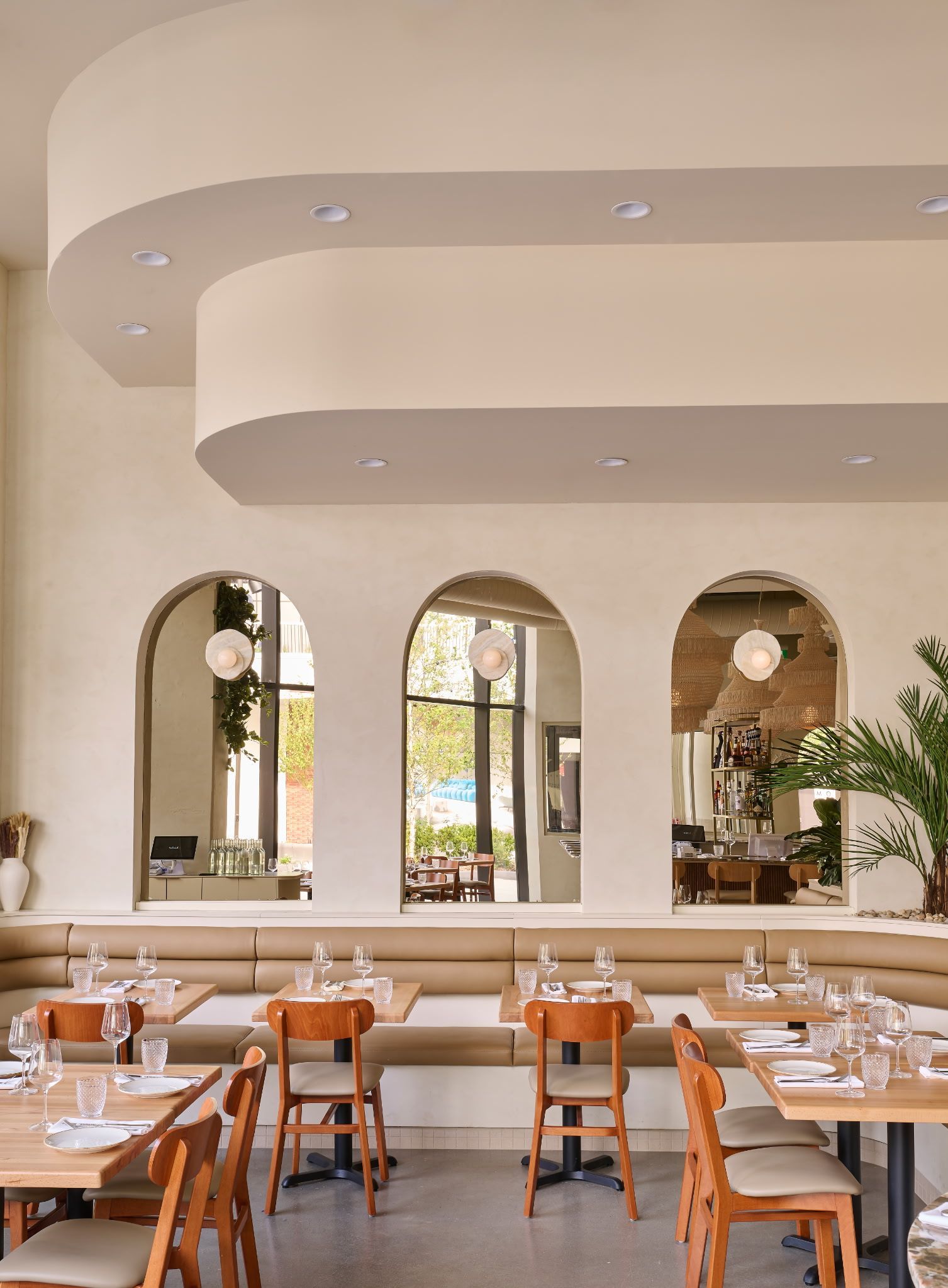 Salle à manger élégante d'un restaurant avec miroirs arqués, murs beiges et tables en bois soigneusement disposées.
