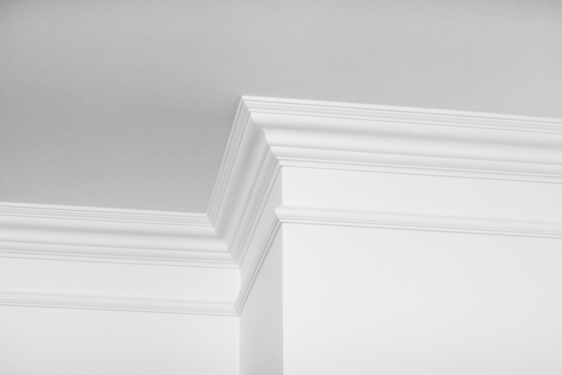 Moulure blanche sur un mur gris clair, révélant un détail d'angle de plafond