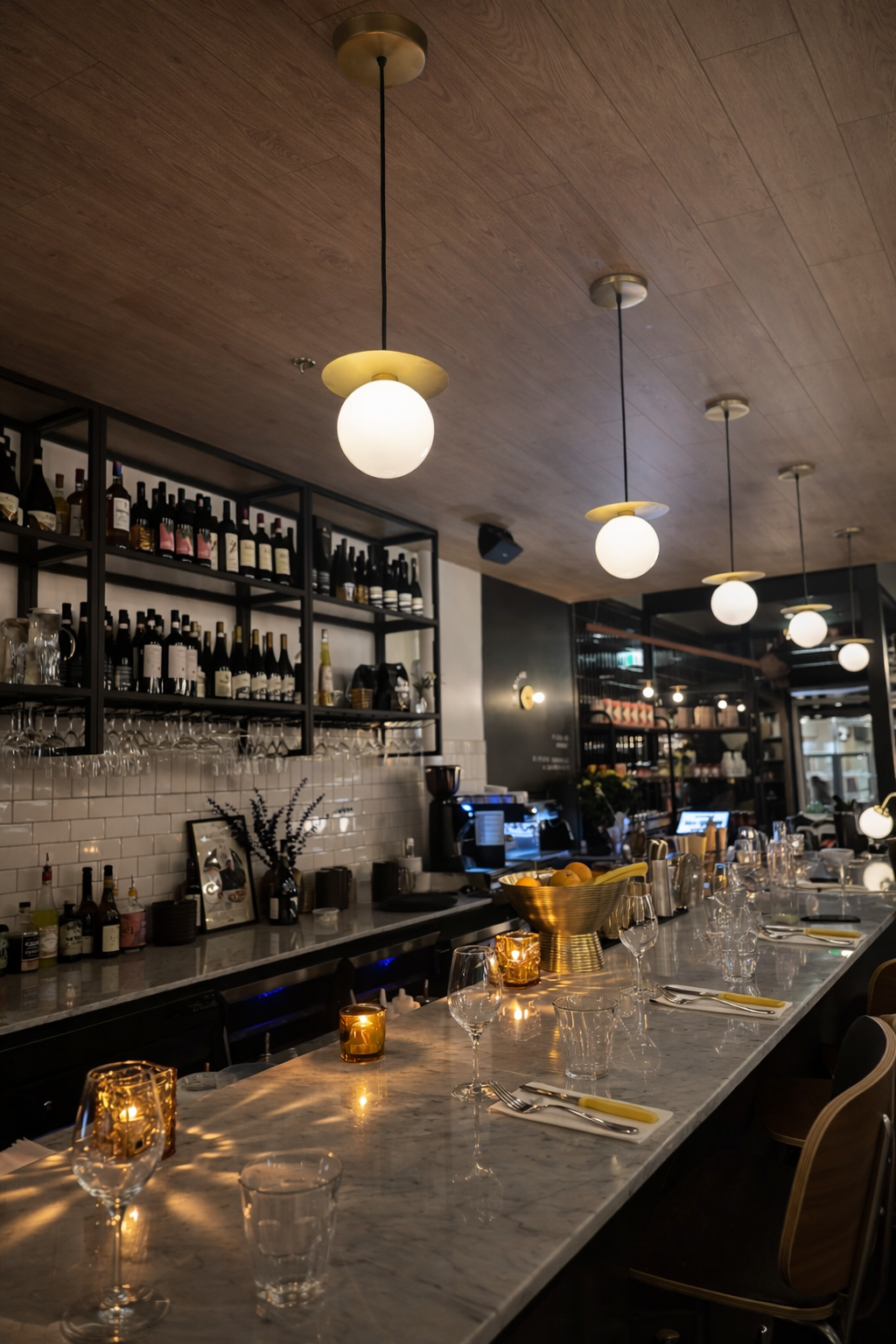 Intérieur de bar à l'éclairage chaleureux, avec des suspensions lumineuses en forme de globe, des étagères à bouteilles et un long comptoir en marbre.