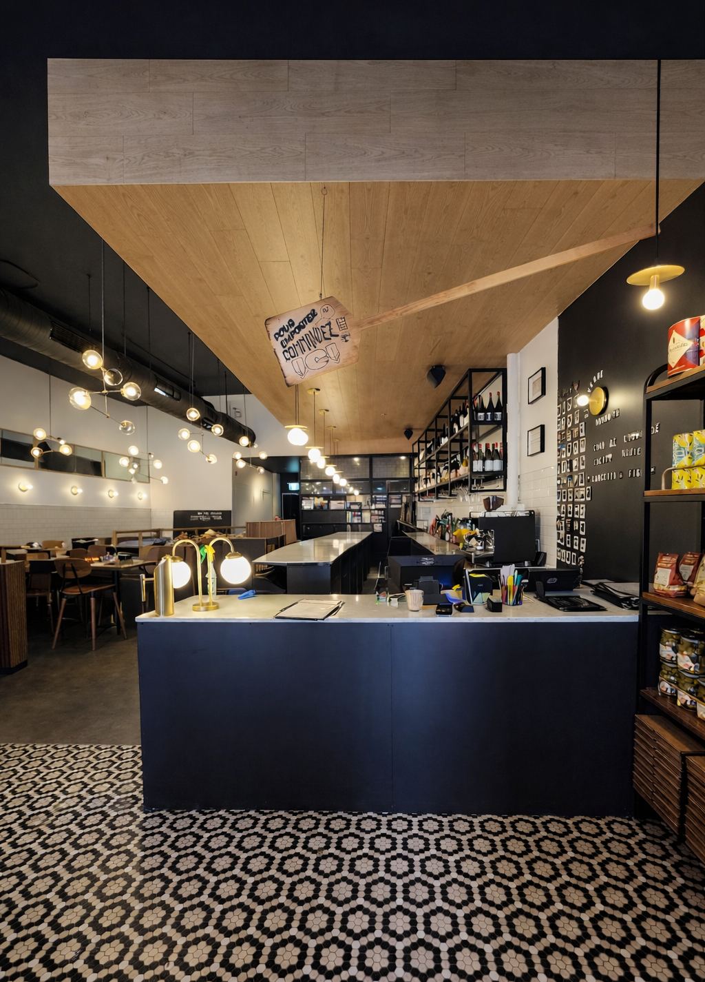 Intérieur de café moderne avec sol en carrelage géométrique noir et blanc, suspensions lumineuses et comptoir de service central.