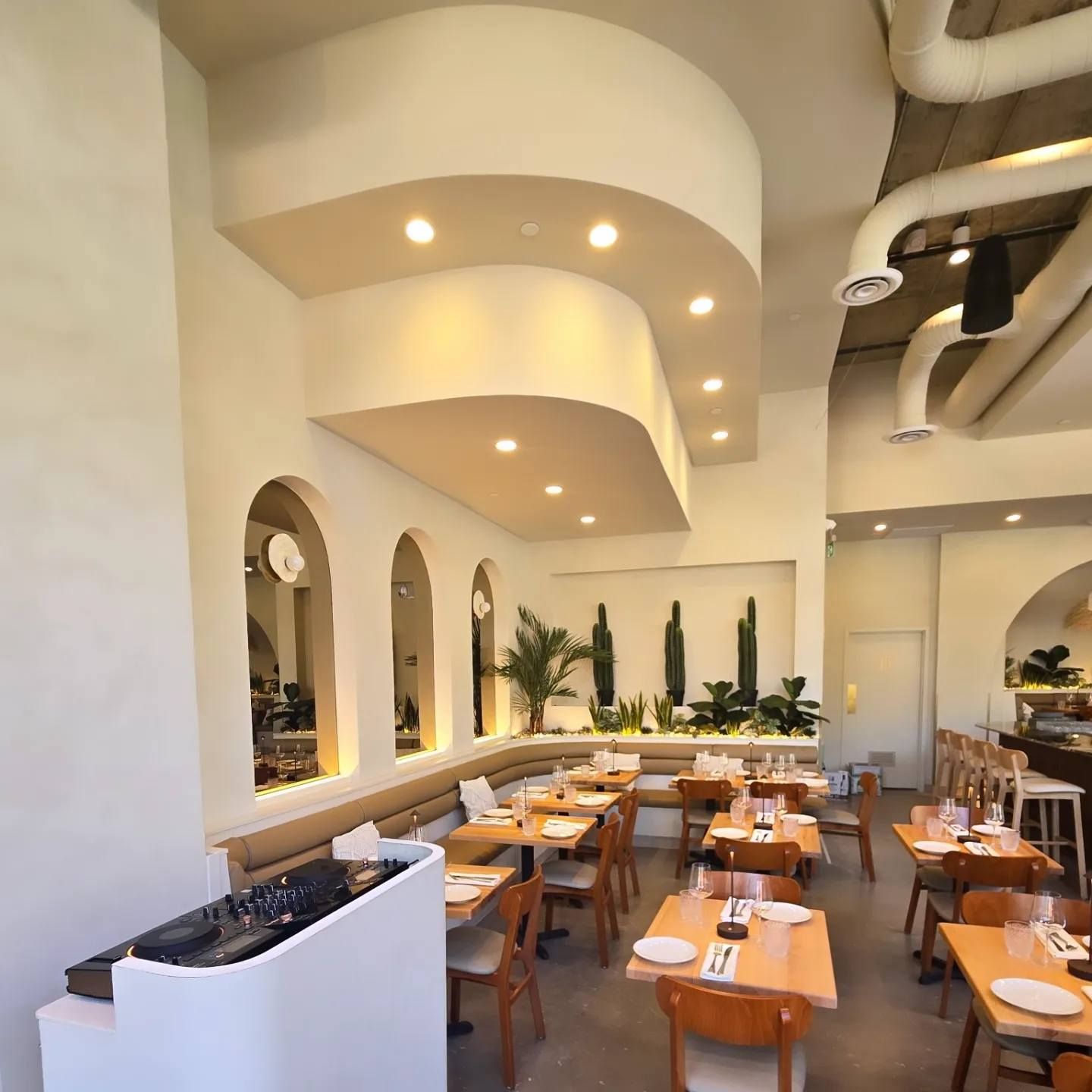 Salle à manger moderne d'un restaurant avec arches blanches, éclairage chaleureux et tables en bois soigneusement disposées.