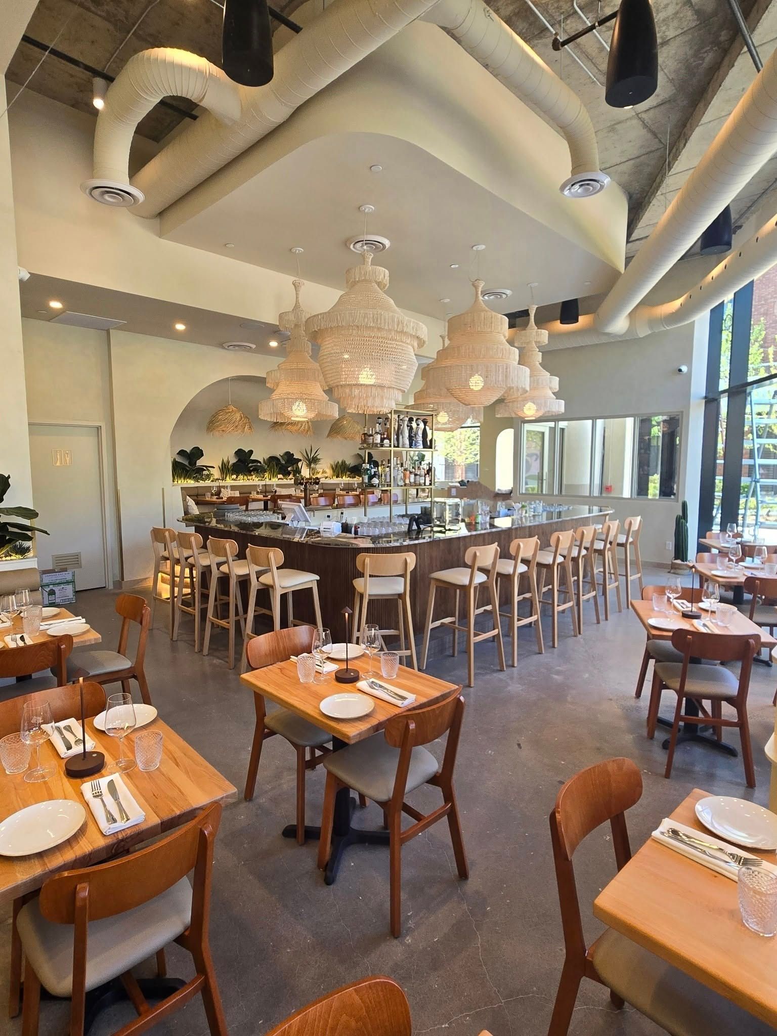 Intérieur de restaurant moderne avec tables en bois, tabourets de bar et grands luminaires suspendus en osier.