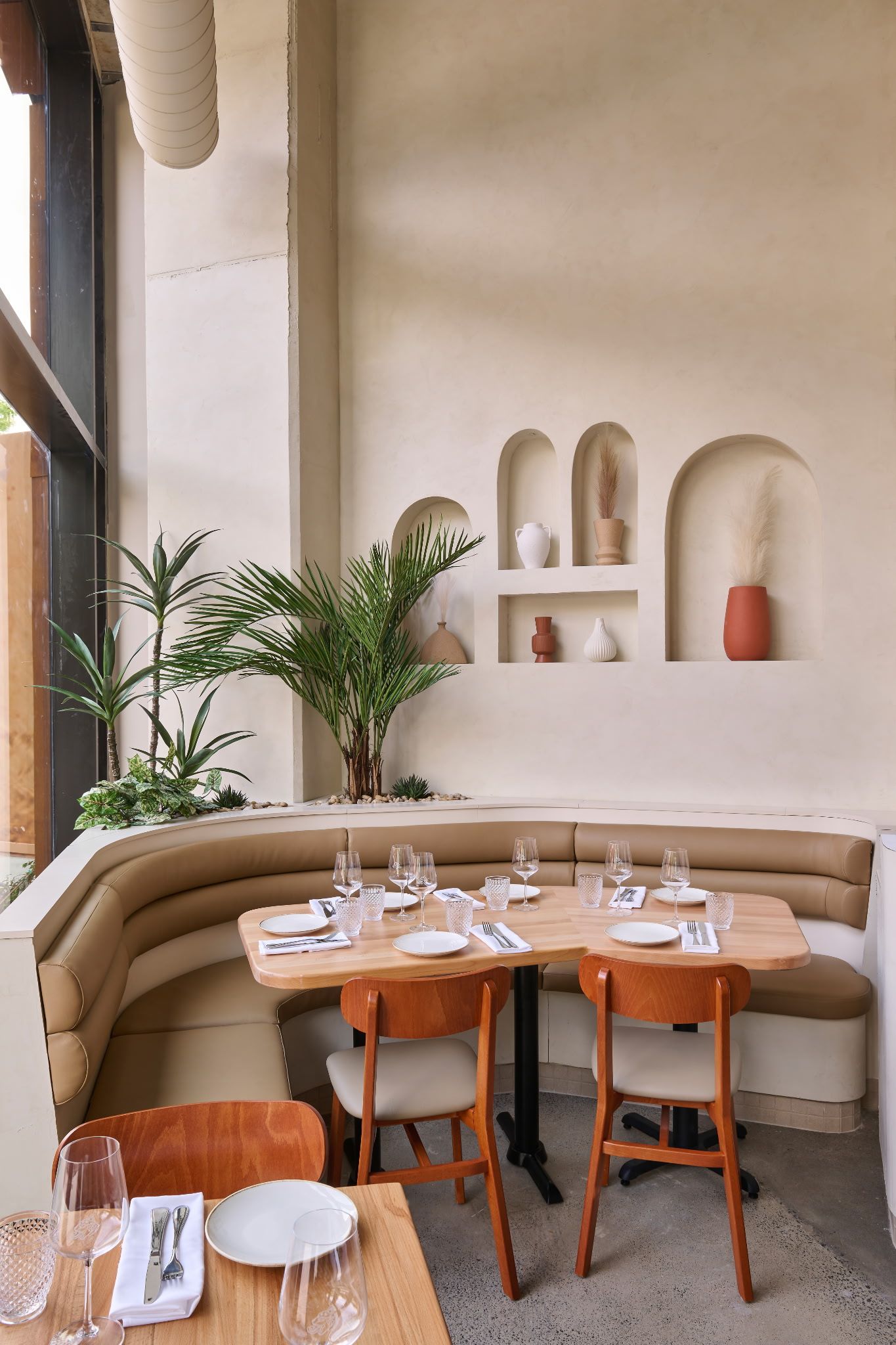 Coin café confortable avec banquette beige, table en bois et étagères dans une pièce aux tons crème doucement éclairée