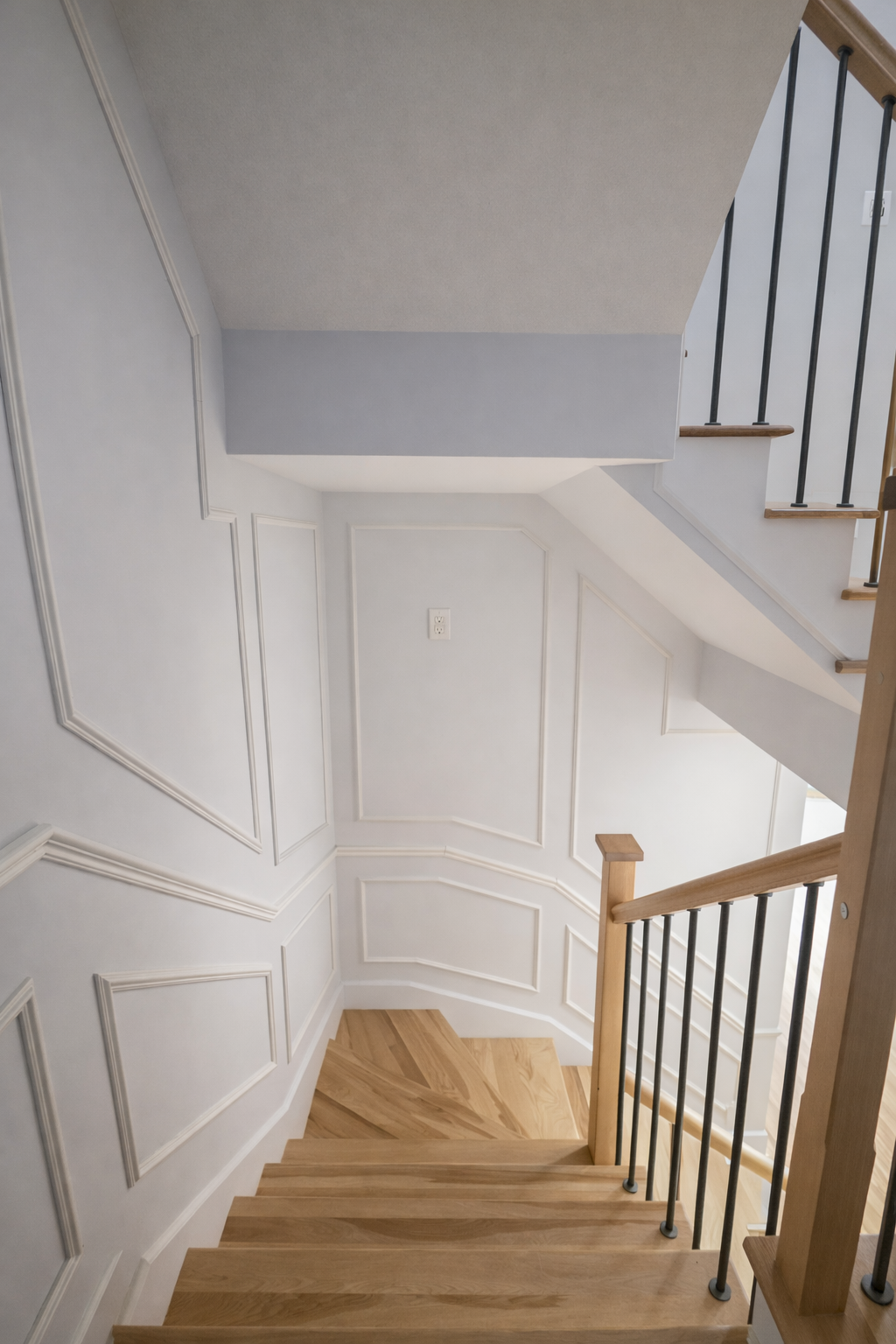 Palier d'escalier avec murs lambrissés blancs, marches en bois et rampe en bois et noir.