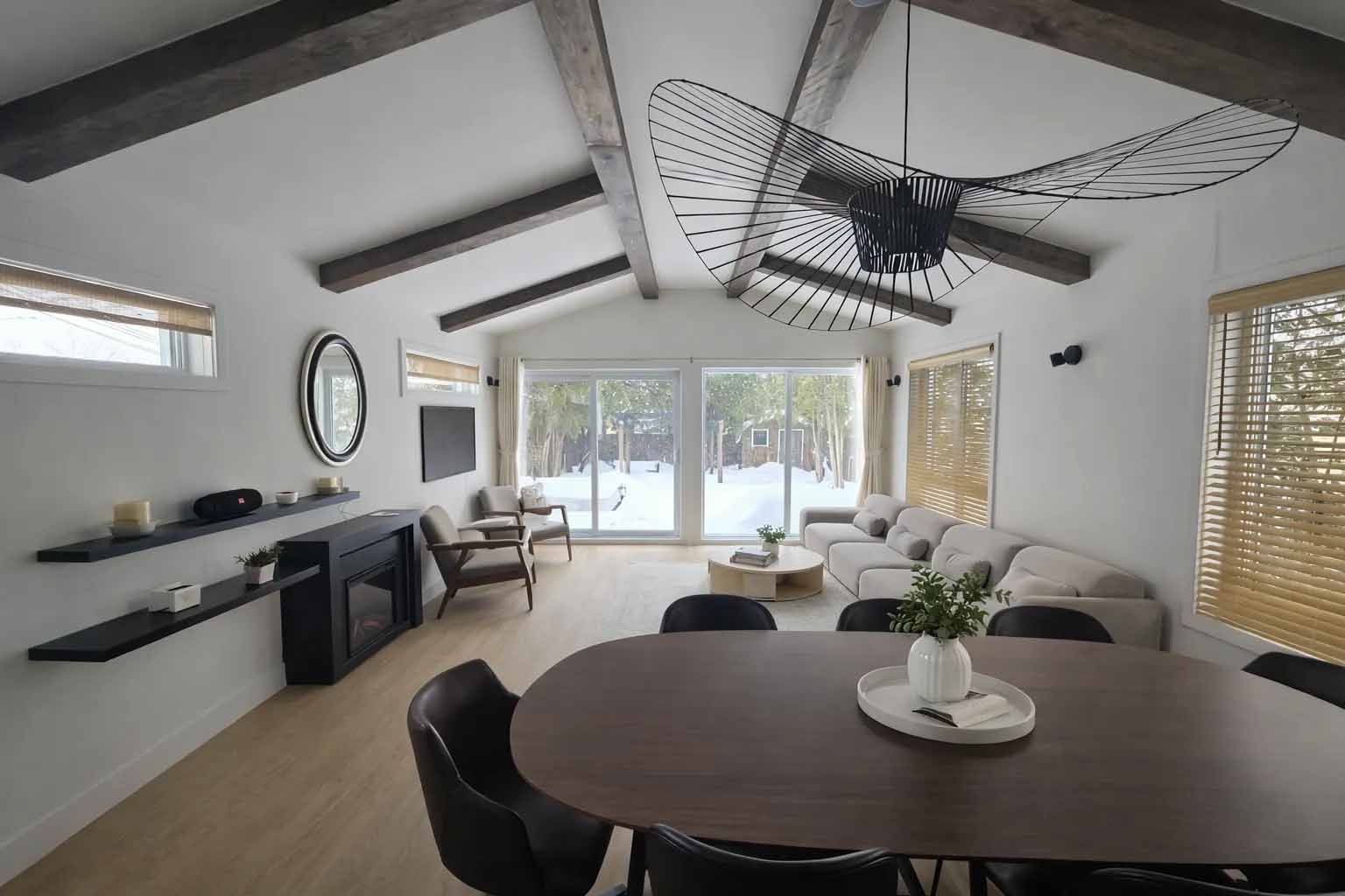 Salon moderne à aire ouverte avec table à manger ronde, canapé, cheminée, ventilateur de plafond et grandes portes coulissantes en verre.