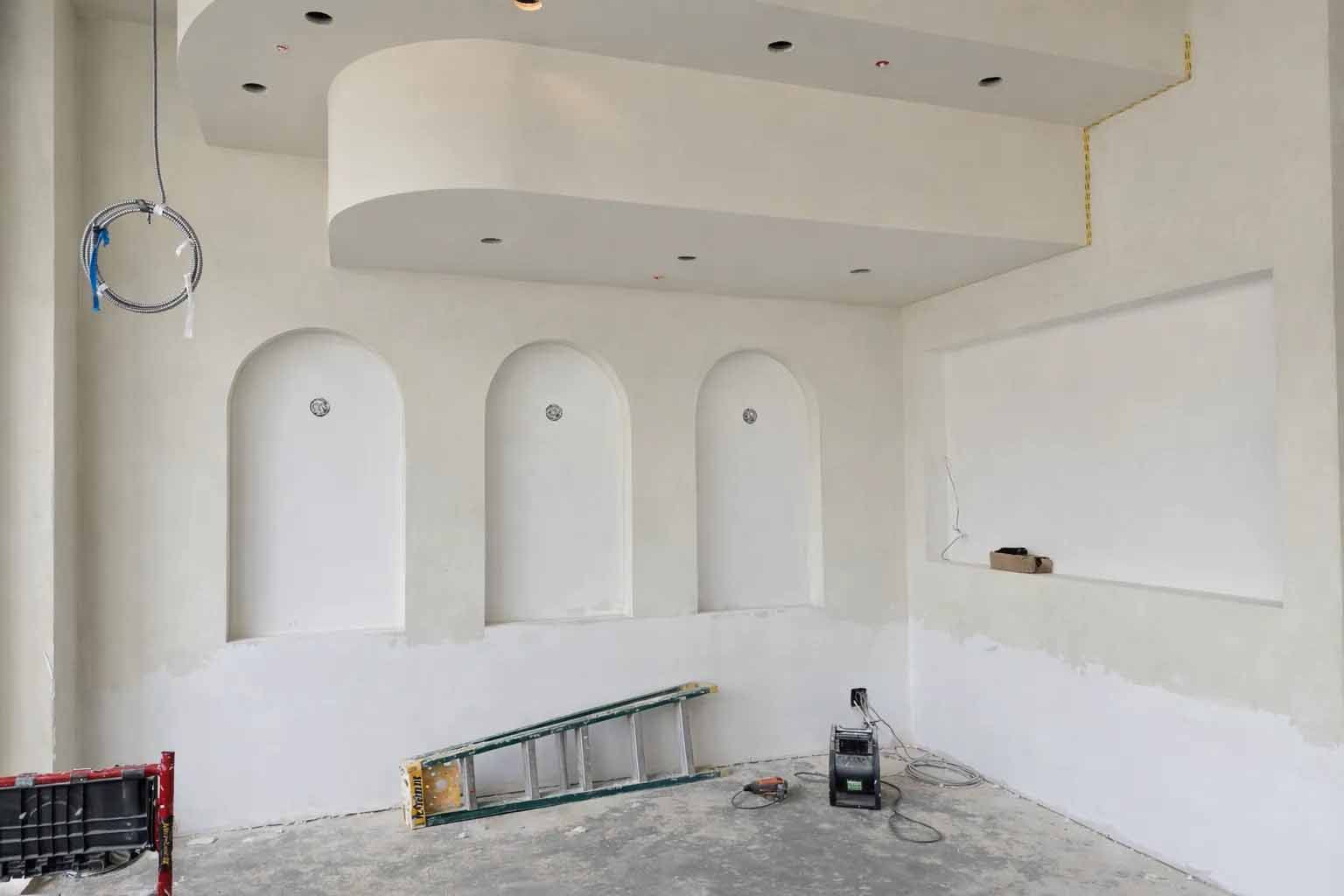 Empty room under renovation with arched wall niches, a ladder, and construction tools on the floor