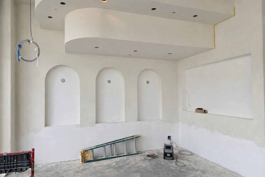 Pièce nue en cours de rénovation avec niches murales blanches intégrées, sol non fini et échelle appuyée contre le mur.