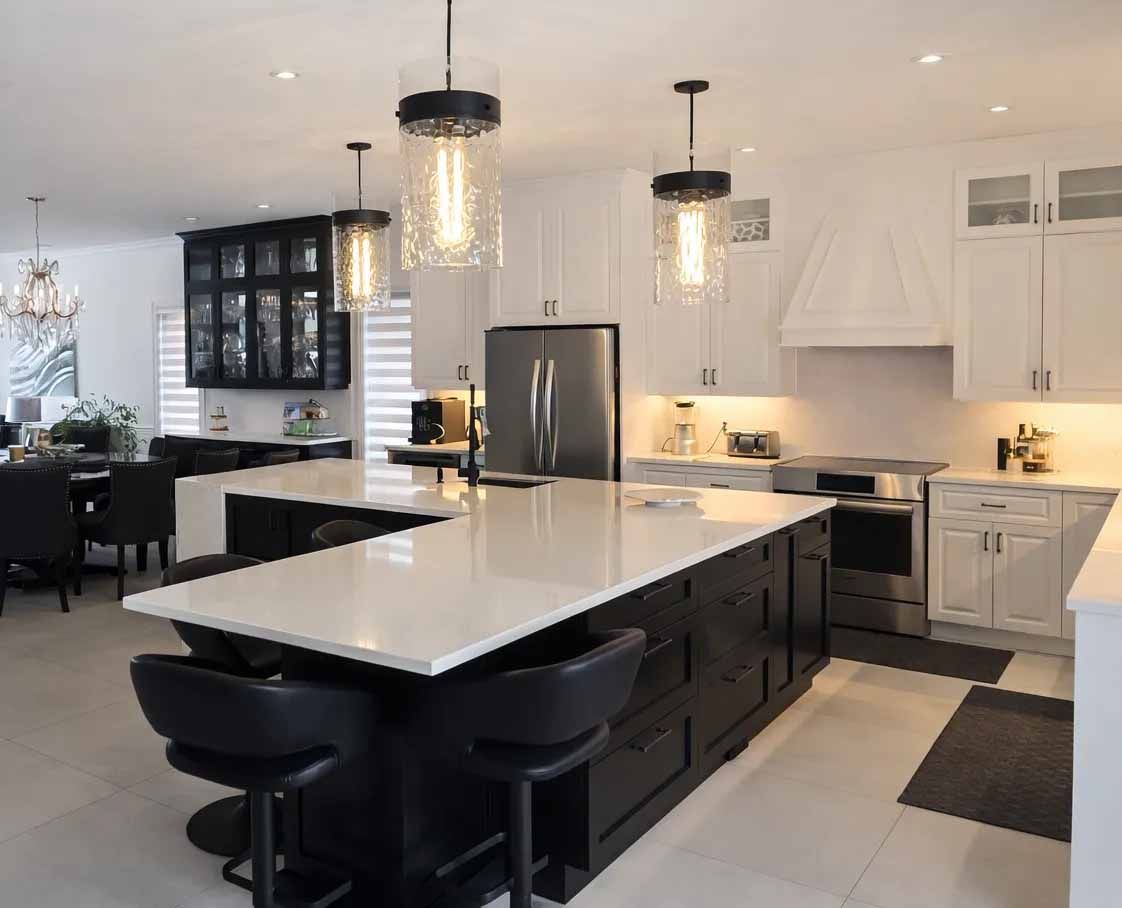 Cuisine moderne blanche et noire avec îlot central, luminaires suspendus et électroménagers en acier inoxydable