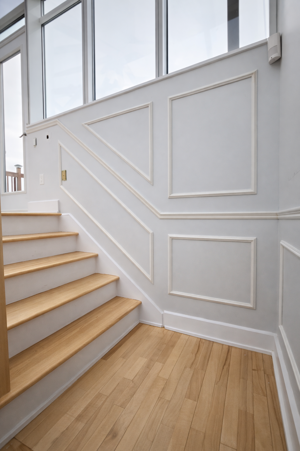 Escalier lumineux avec mur lambrissé blanc, grandes fenêtres et parquet clair