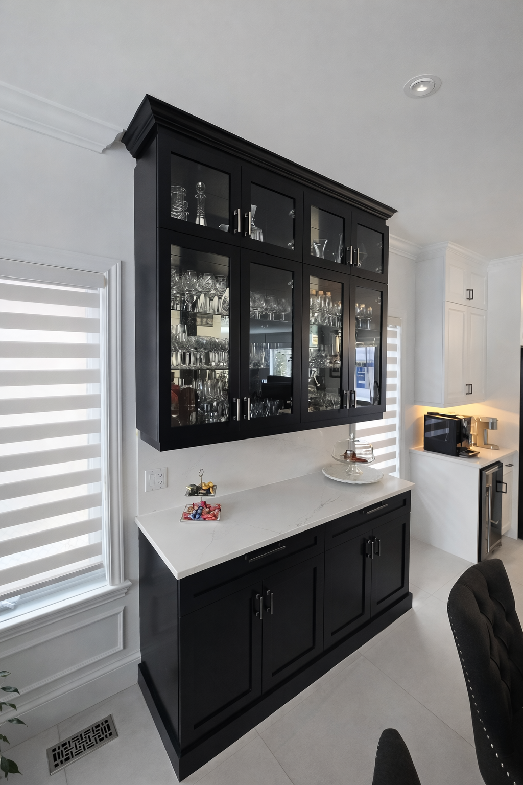Buffet noir avec vitrines et plan de travail blanc dans une salle à manger lumineuse, à côté d'une fenêtre et d'une petite table d'appoint