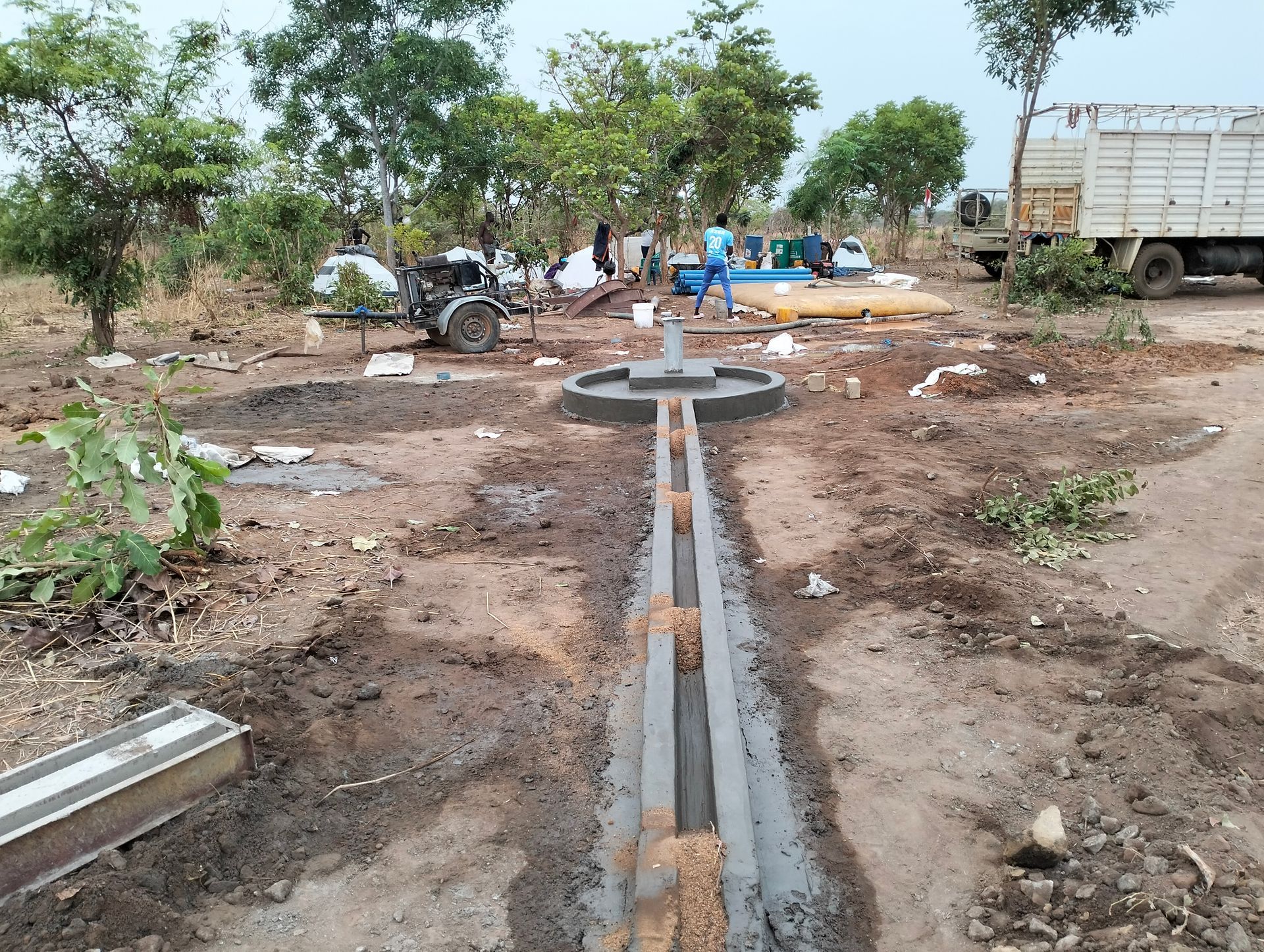 Open concrete drainage channel under construction in a dry rural area with workers and a truck nearby