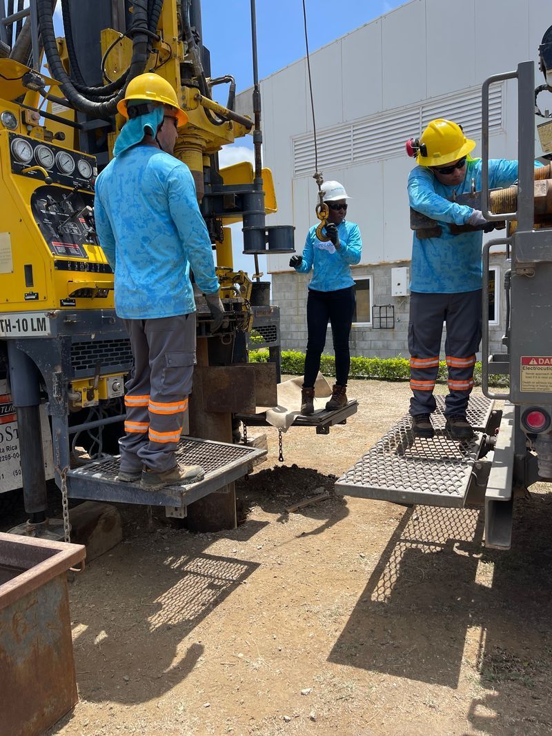 Construction workers in blue uniforms and yellow hard hats operating equipment on a muddy site