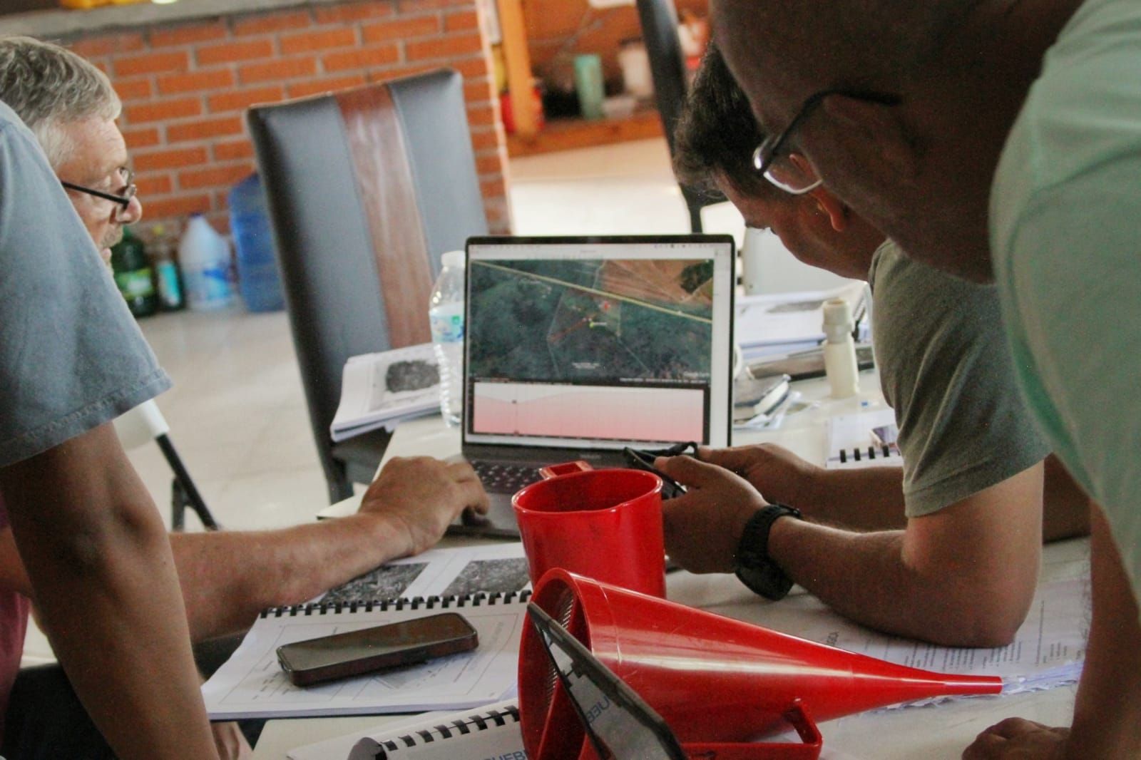 Two people leaning over a laptop on a table, with a red cup and notebook in the foreground