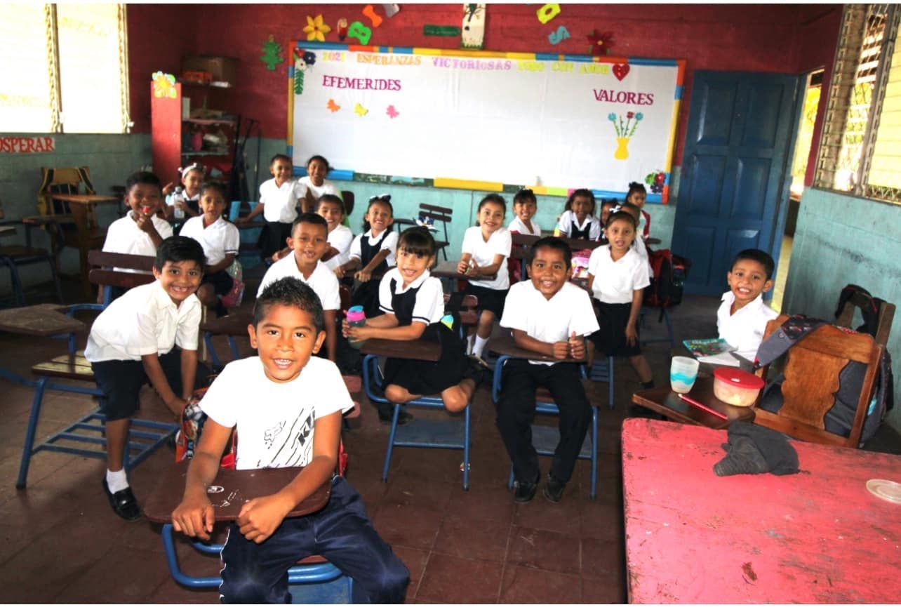 Students seated at desks in a colorful classroom, facing the camera and smiling