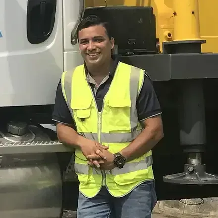 Person in a neon yellow safety vest standing beside a large truck, smiling in an industrial setting