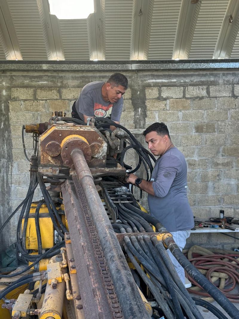 Two workers inspecting large rusted machinery with hoses in an industrial workshop