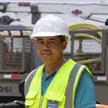 Worker in white hard hat and neon safety vest standing in front of industrial machinery
