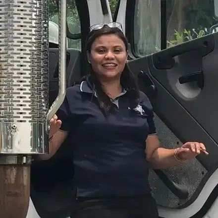 Woman smiling beside a metallic industrial machine outdoors, wearing a dark polo shirt.