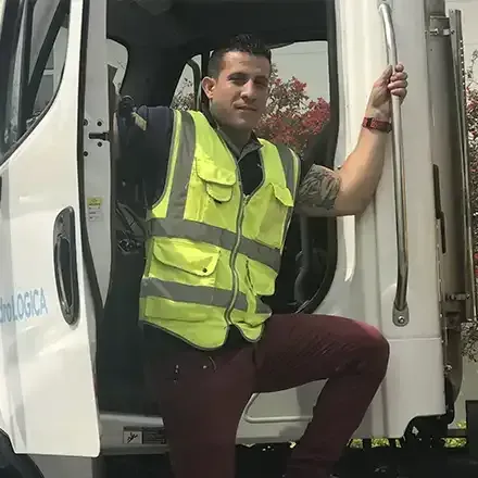 Worker in a neon yellow safety vest standing in a white truck doorway, holding the door handle.