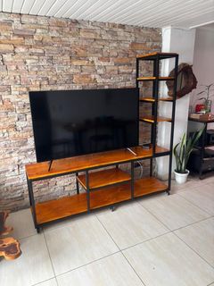 Un televisor sobre un soporte de madera contra una pared de ladrillos, con una estantería alta negra