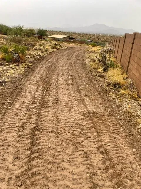 A dirt road in the desert with a fence in the background.