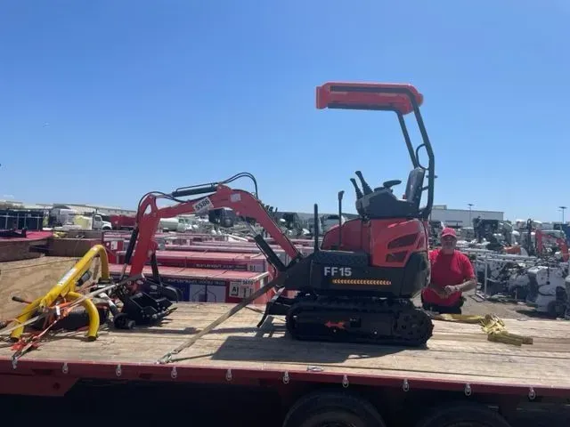 A small excavator is sitting on top of a flatbed truck.