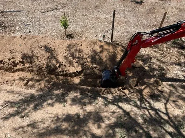 A red excavator is digging a hole in the dirt.