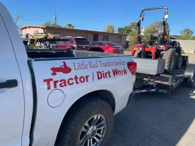 A little red tractor service truck is towing a tractor on a trailer