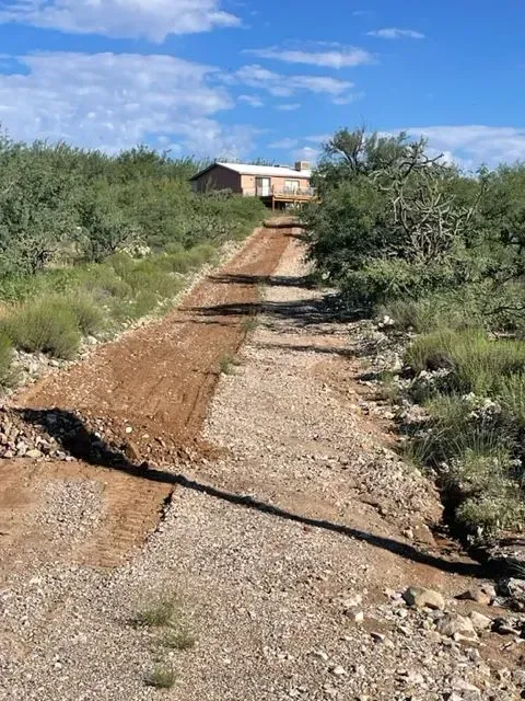 A dirt road leading to a house in the middle of a field.
