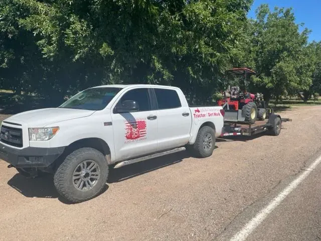 A white truck is towing a tractor down a road.