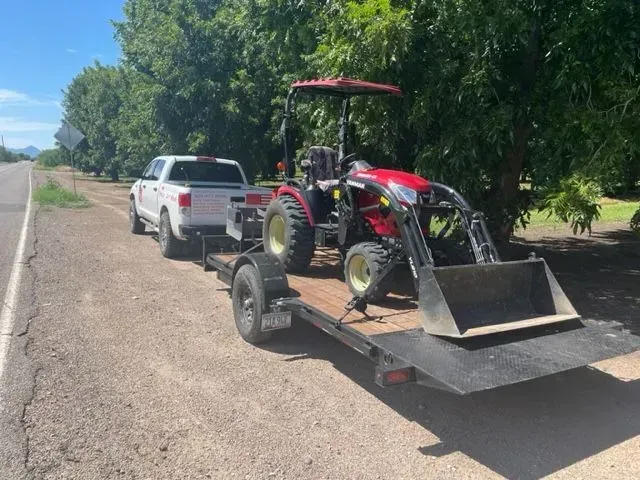 A tractor is being towed by a truck on a trailer.