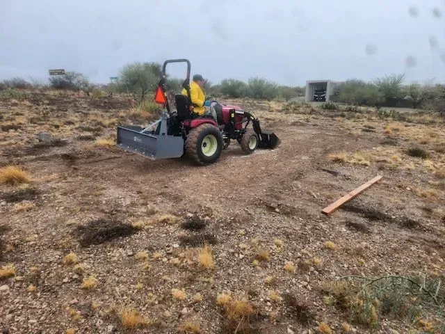 A man is driving a tractor in a dirt field.