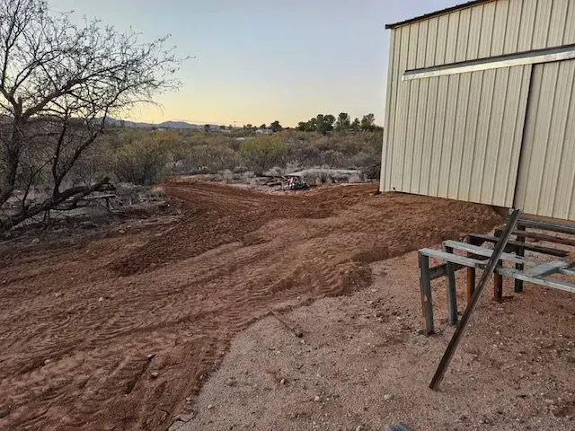 A shed is sitting in the middle of a dirt field.