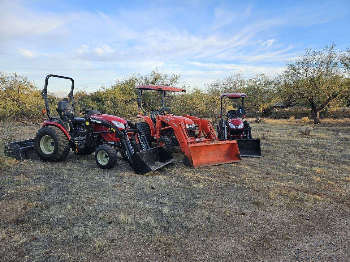Three tractors are parked in a field with trees in the background.