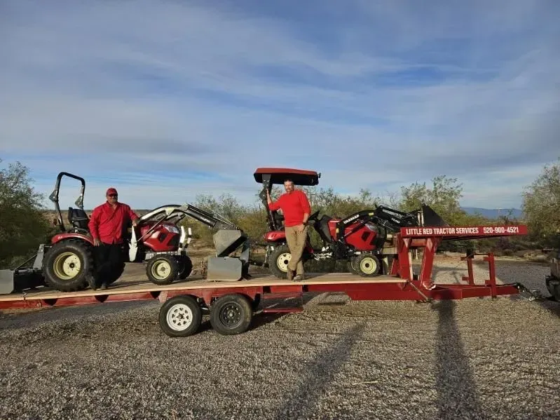 A man is standing next to two tractors on a trailer.