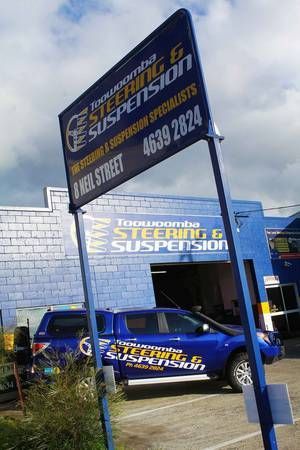 Blue auto repair shop and truck with “steering & suspension” signage and phone number outdoors