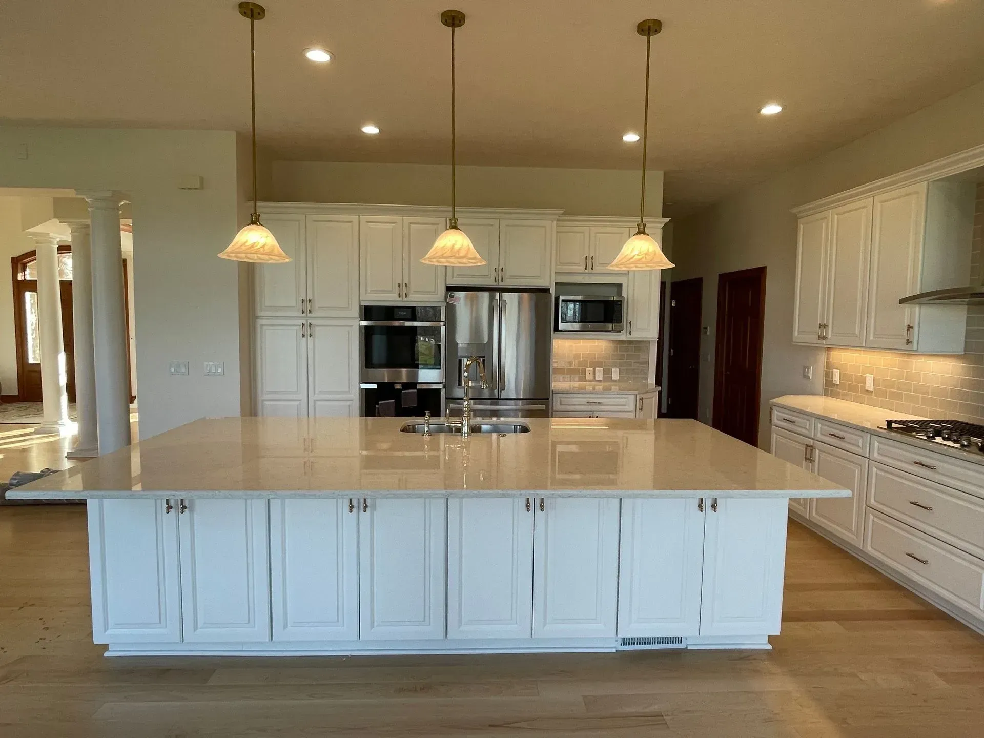 Bright white kitchen with large island, stainless steel appliances, and pendant lights.