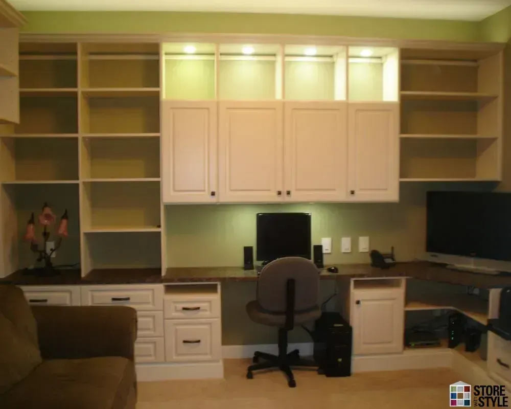 Built-in white desk and shelving unit with a computer, chair, and cabinets, in a home office.