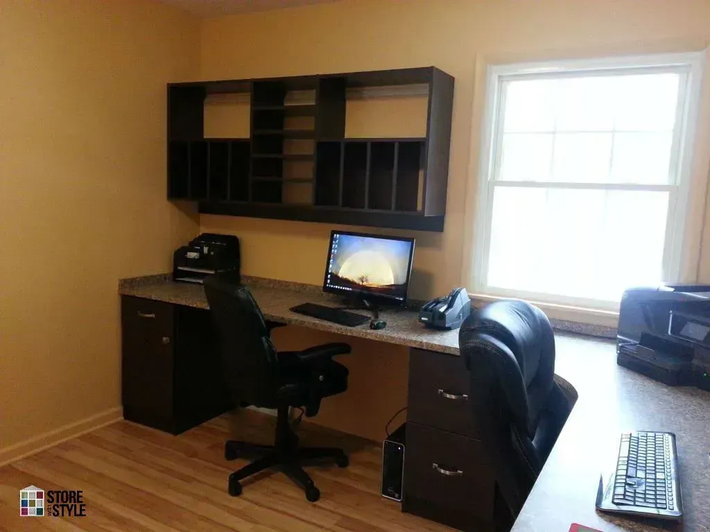 Dark brown desk with computer, chair, and shelf against tan wall by window.