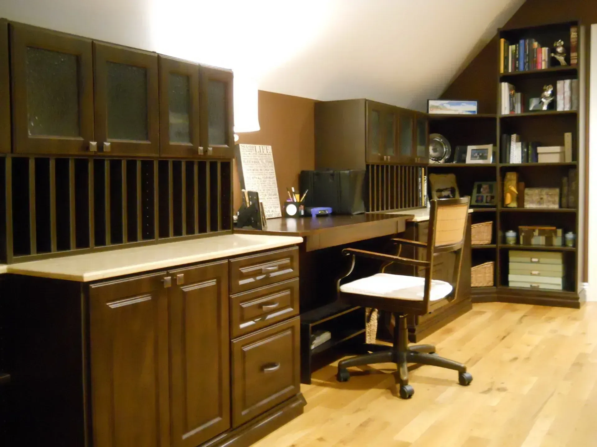 Dark wood office space with desk, chair, cabinets, and bookshelf on hardwood floor.