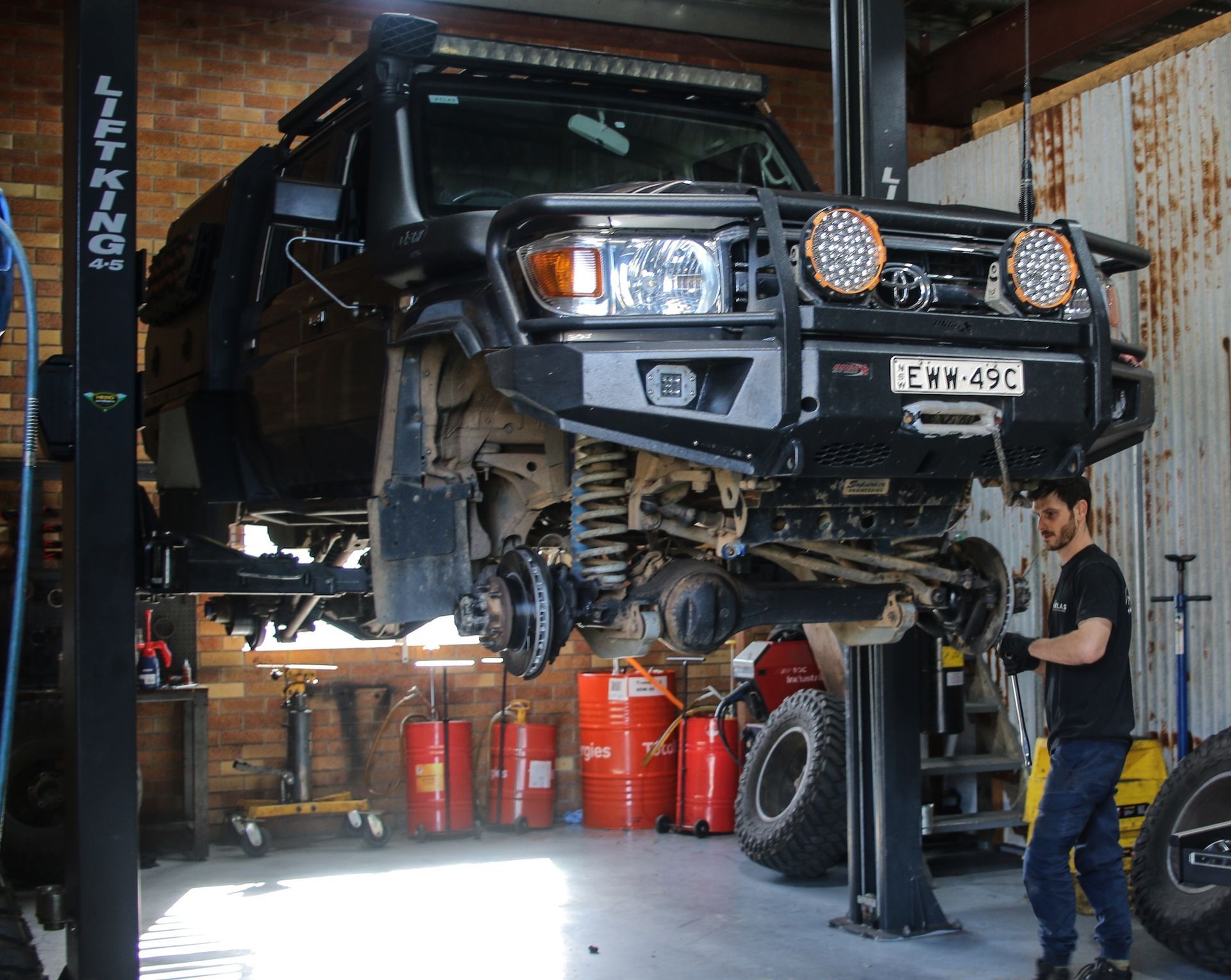SUV raised on a lift in an auto garage, with a mechanic working nearby and tools in the background