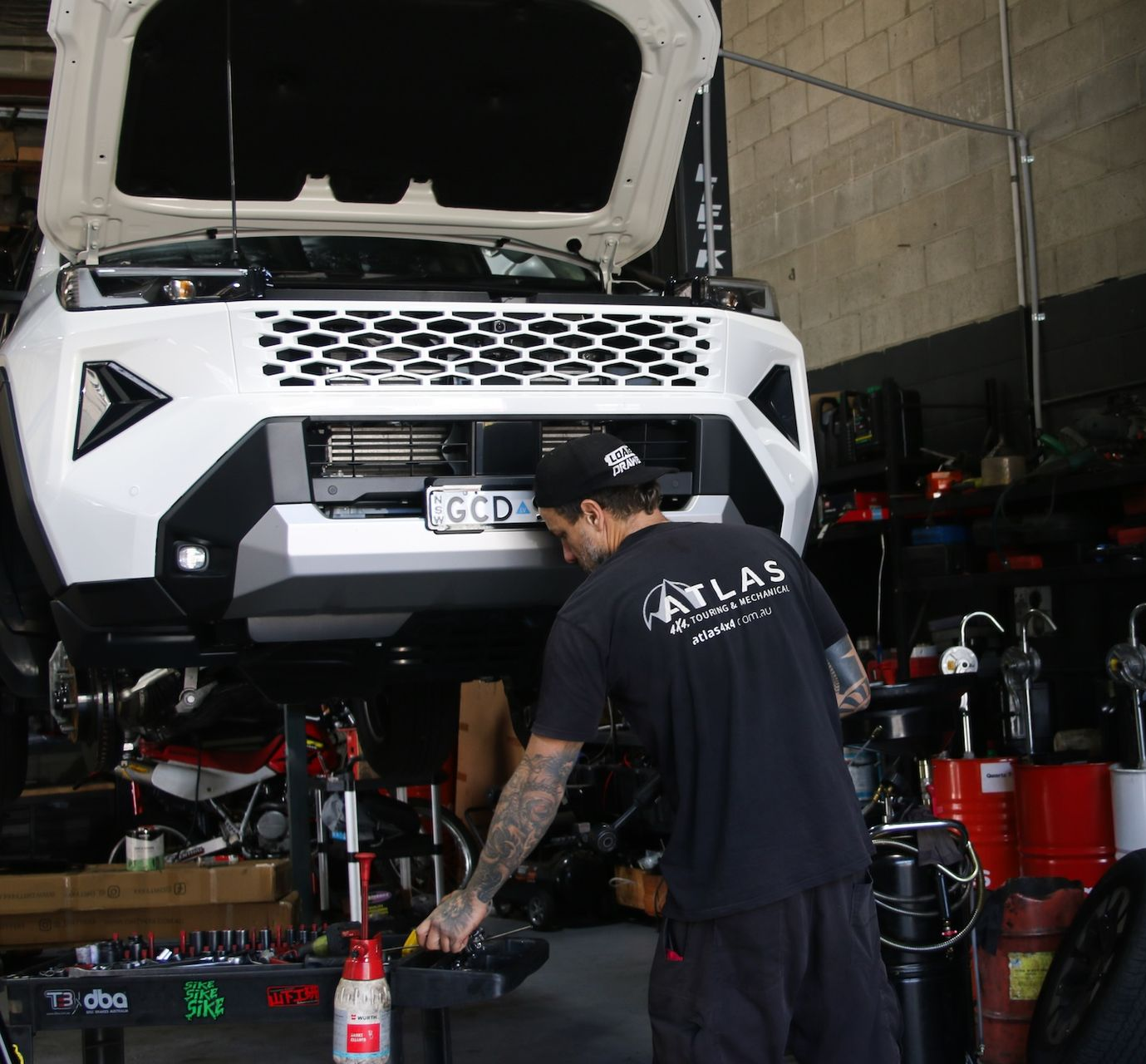 Mechanic working on a white SUV with its hood open in a busy auto shop