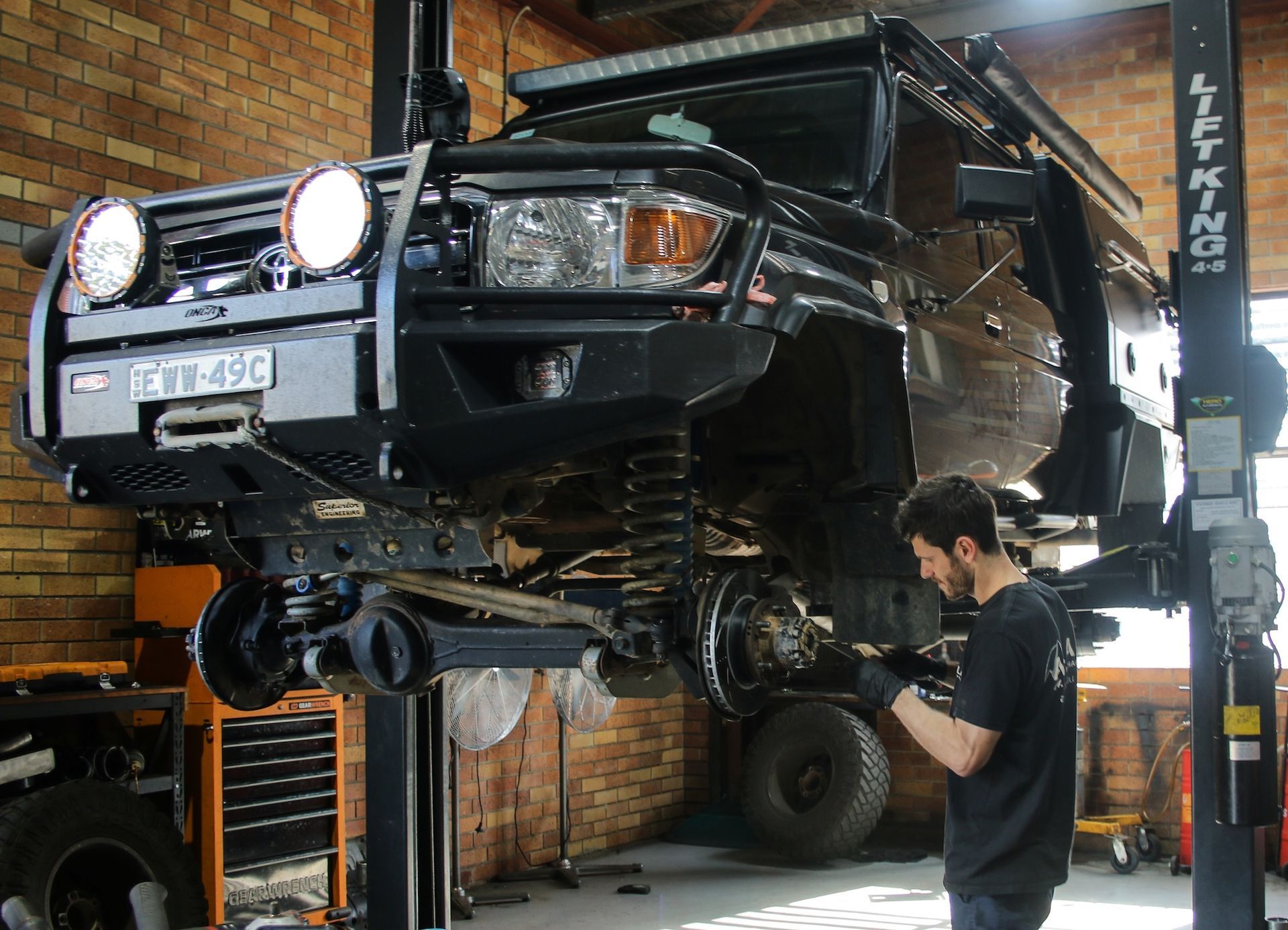 Black lifted SUV in auto garage with mechanic working underneath